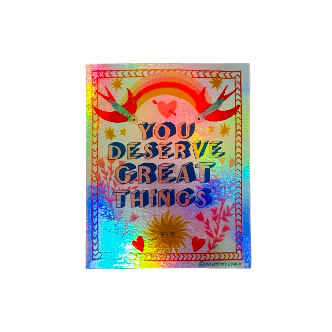 A holographic sticker with the phrase "You Deserve Great Things" surrounded by a rainbow, birds, hearts, and a sun illustration.