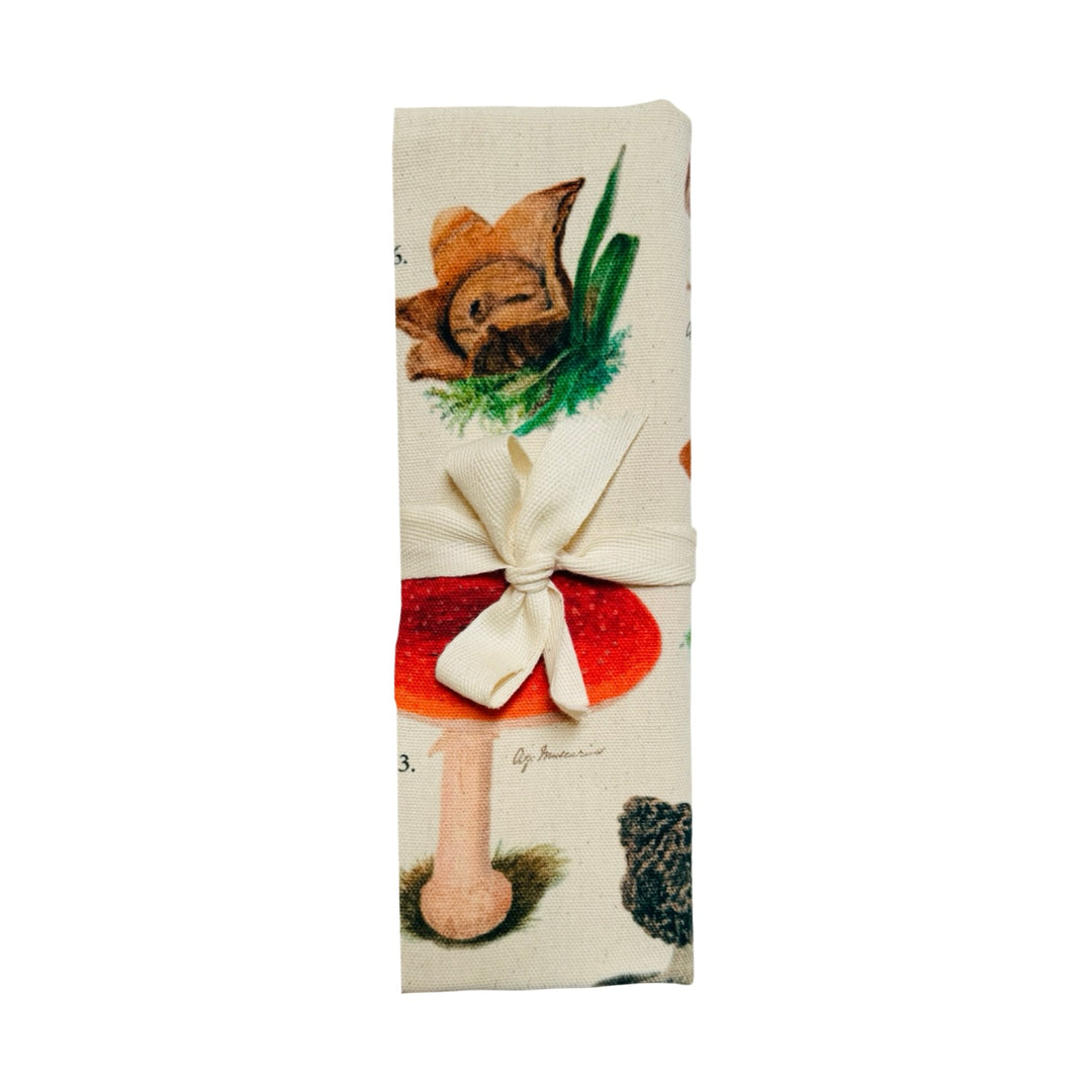 Tea towel featuring a vintage-style botanical chart of illustrated mushrooms labeled with the title “Fungi” folded in half tied with a ribbon. 