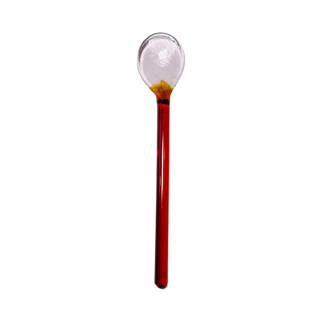 A glass stirring spoon with a pink and amber color variation, featuring a rounded scoop and a slender handle.