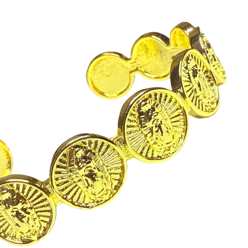 A close up view of a gold-tone cuff bracelet with repeating round Our Lady of Guadalupe medallions.