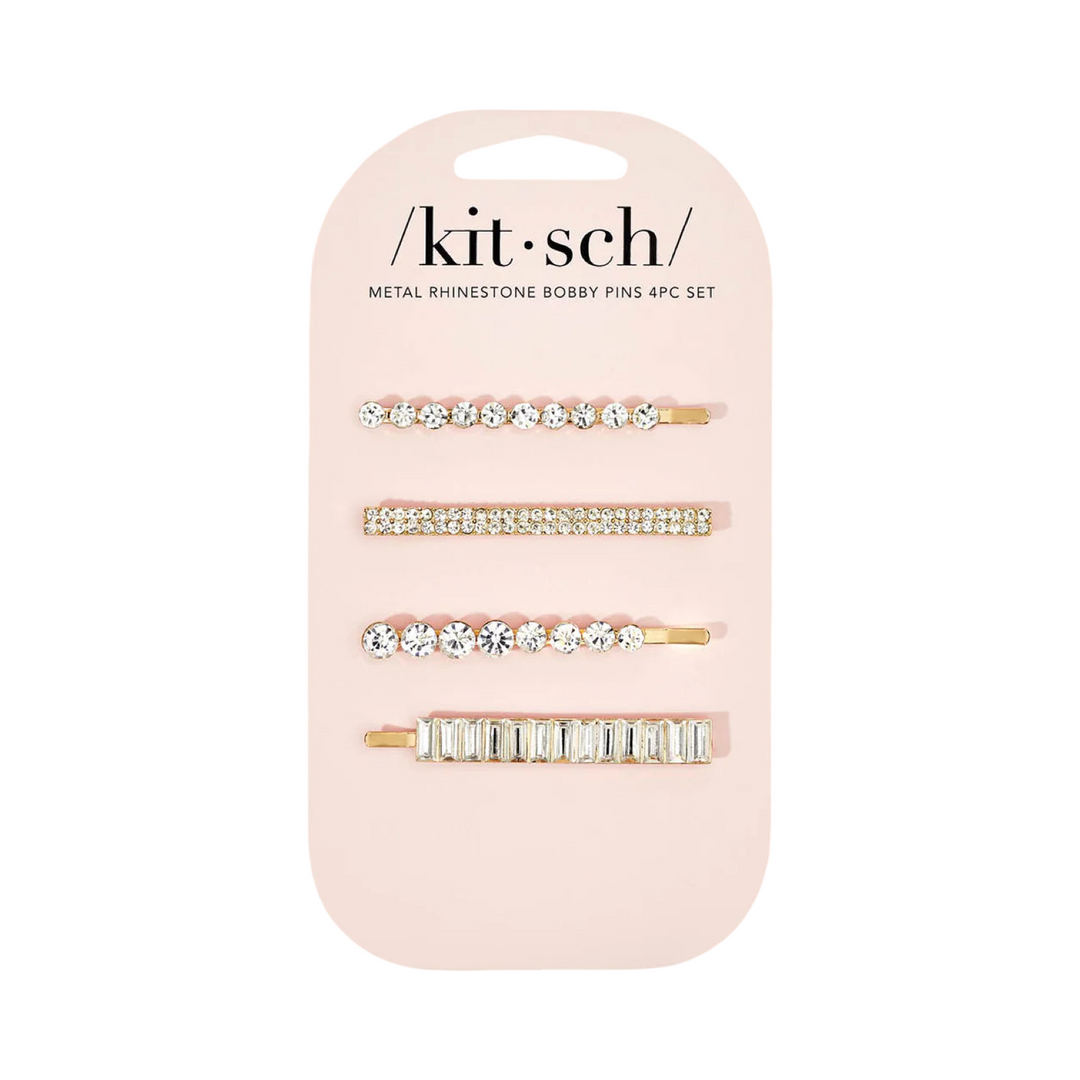 Four gold metal bobby pins with assorted rhinestone designs on a branded display card.