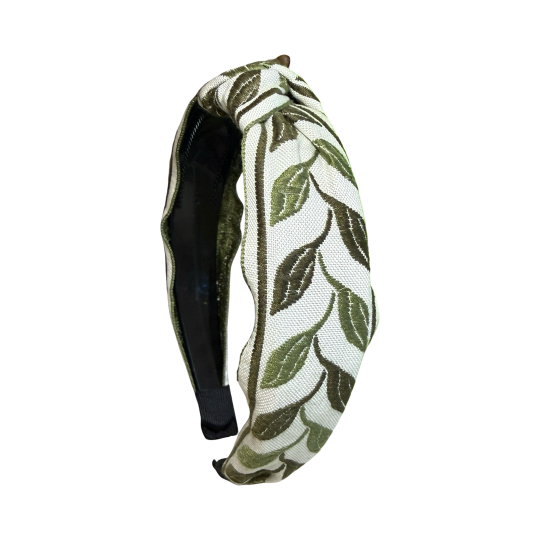 A knotted fabric headband with an olive green embroidered leaf pattern on a cream background.
