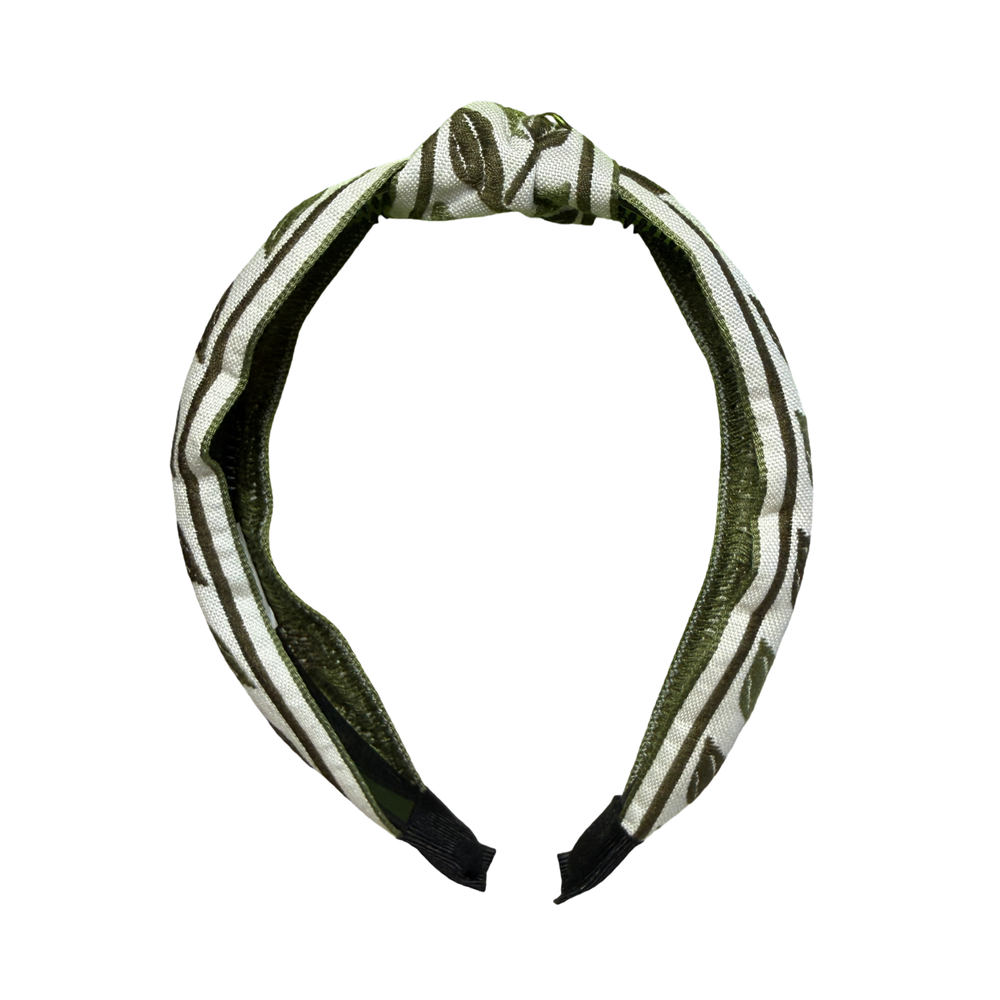 Front view of a knotted fabric headband with an olive green embroidered leaf pattern on a cream background.