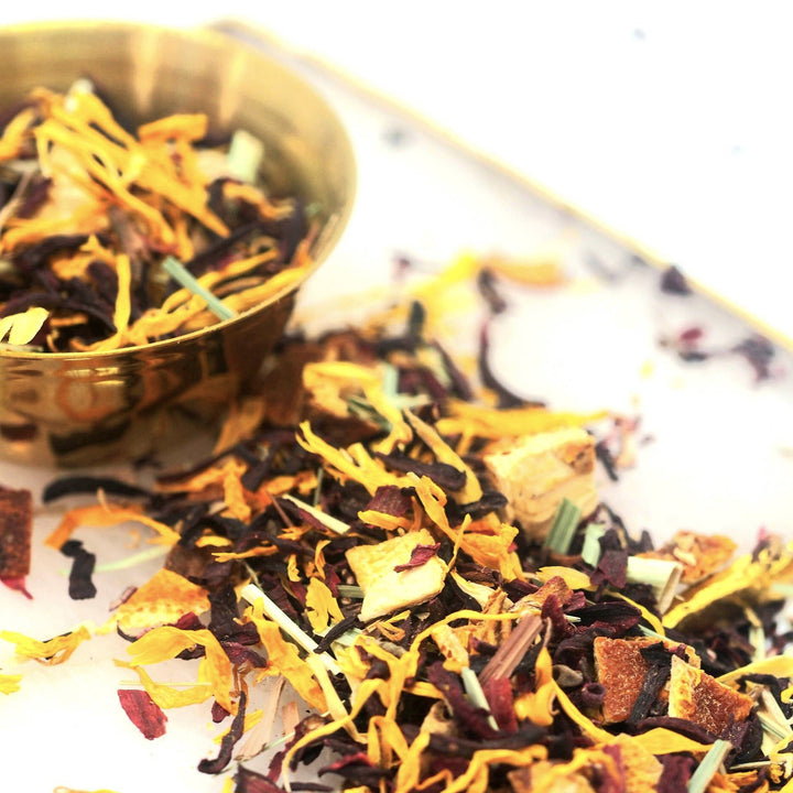 Close up view of dried hibiscus flowers, yellow calendula and orange peels in a gold bowl. Brand: Loveyenergy & Blessings