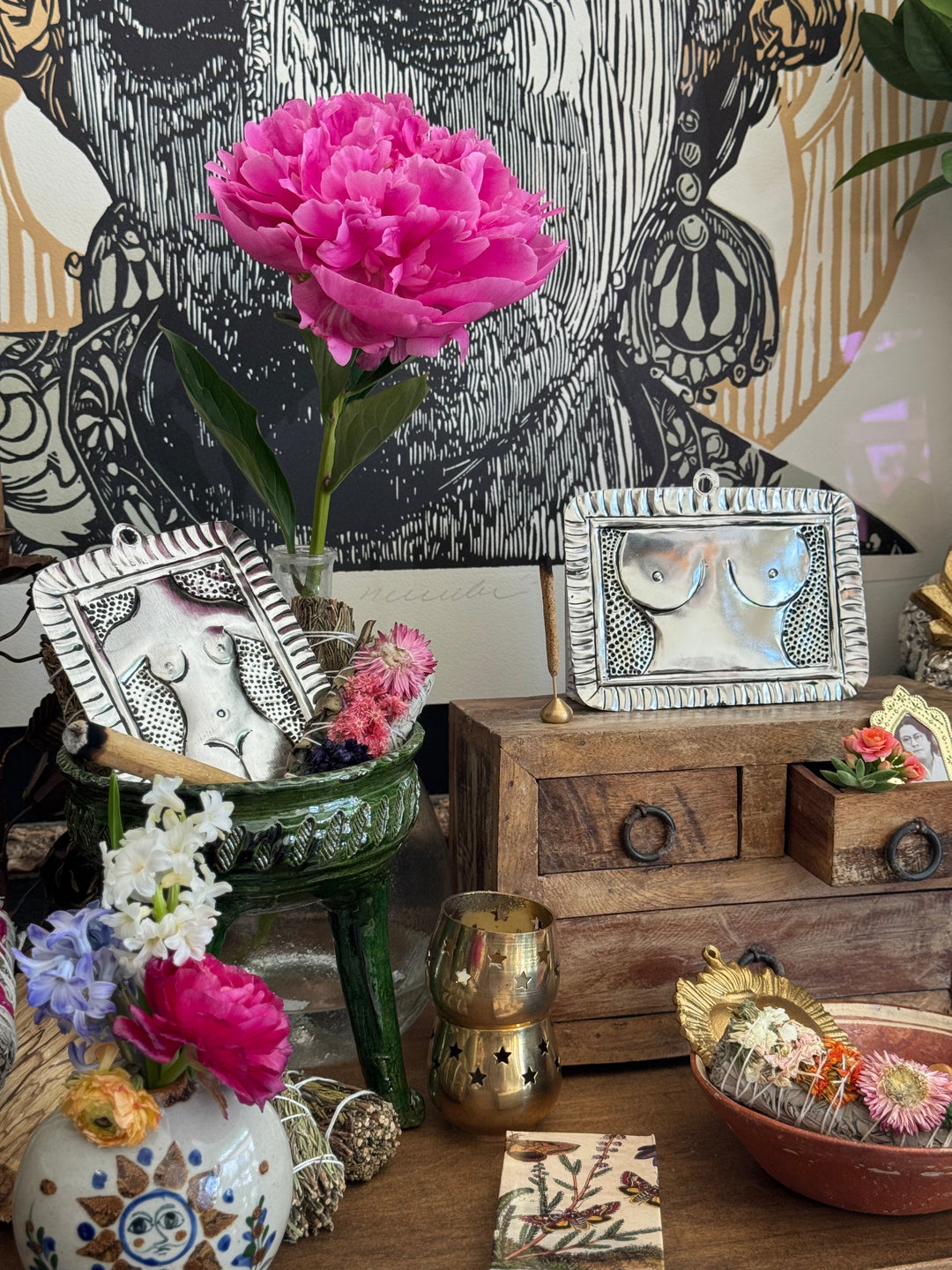 Decorative setting with flowers, a wooden cabinet, and decorative items against a patterned wall.