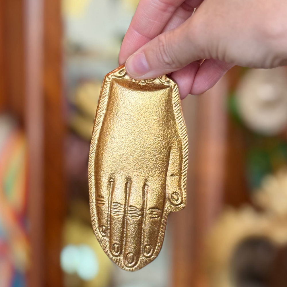 Gold hand-shaped ornament held by a hand with a blurred background