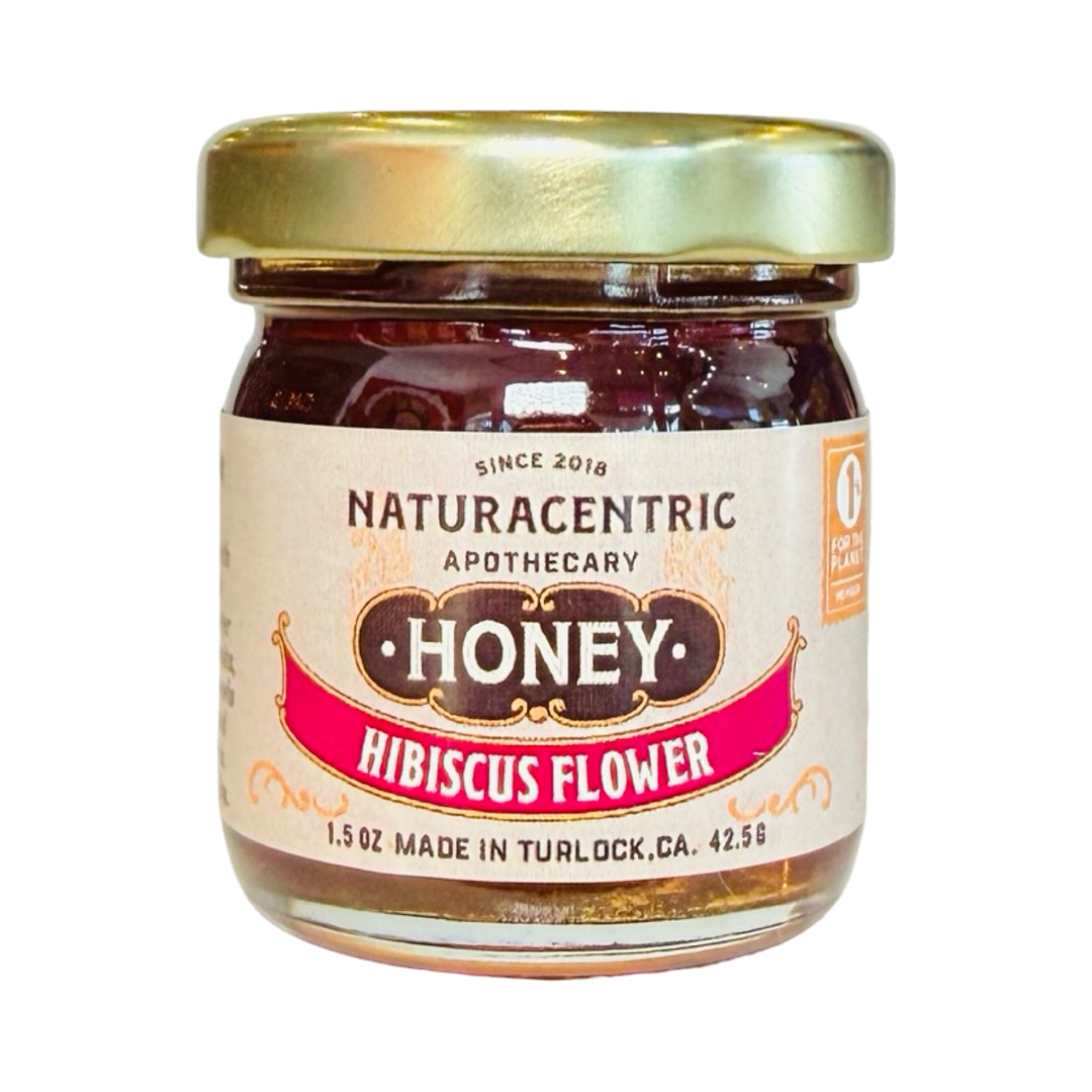 A small 1.5 oz glass jar of Naturacentric Apothecary Hibiscus Flower infused honey with a gold lid, showing a deep red honey color through the glass