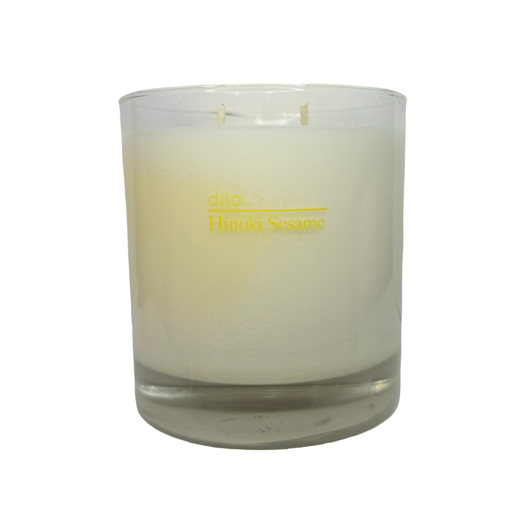 Clear glass containing ivory candle features a yellow branded label on the front.
