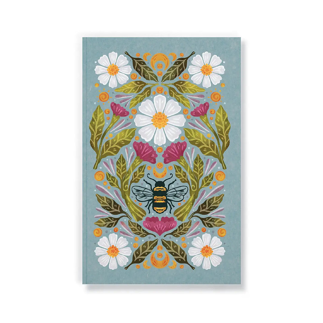 Blue journal with a central honeybee surrounded by white daisies, pink flowers, and green leaves in a folk-art style