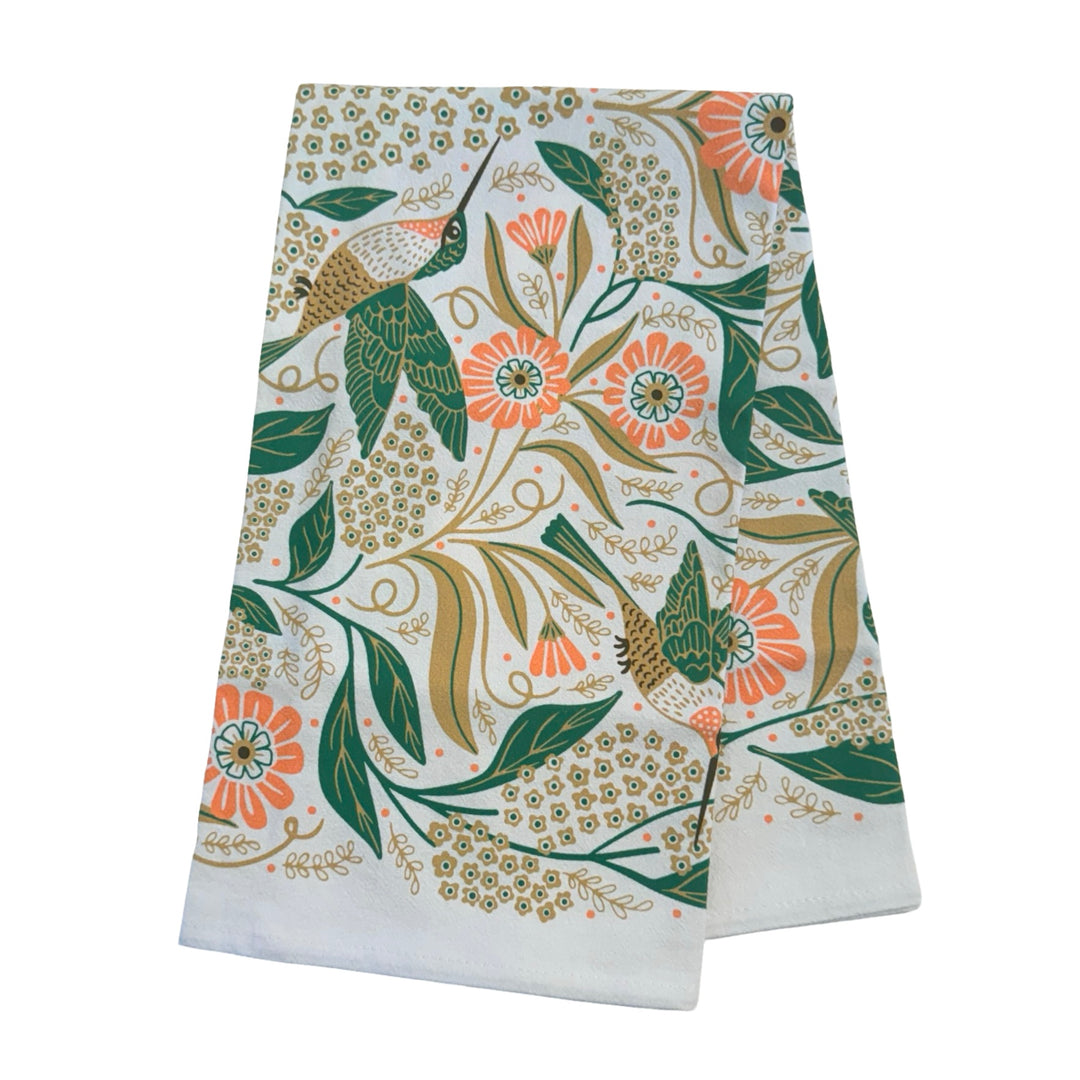 A White kitchen towel with a symmetrical floral and hummingbird design in shades of green, pink, and gold folded in quarters.