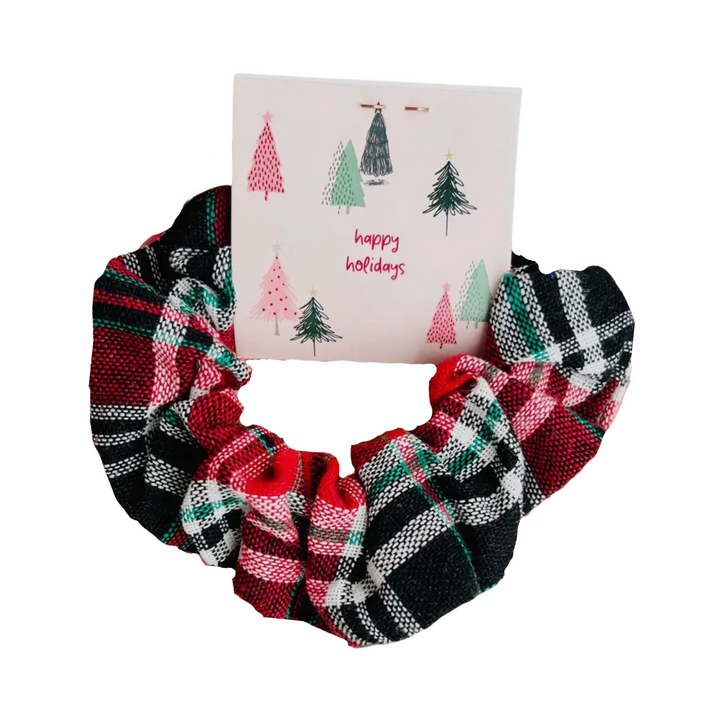 A festive plaid scrunchie in red, green, and white patterns, paired with a card that reads “In my holly jolly era” featuring whimsical holiday tree illustrations. 