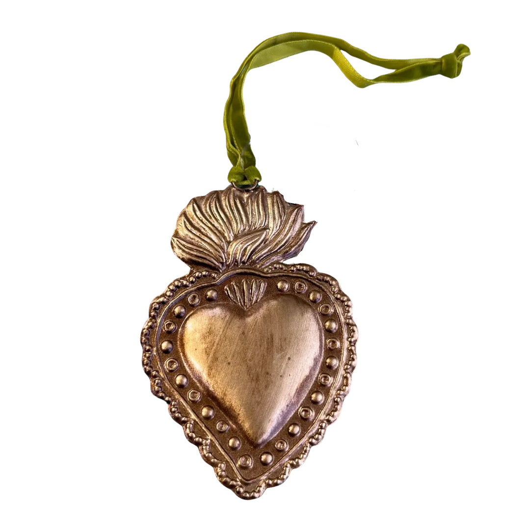 A gold-toned sacred heart ornament with intricate raised details and a flame design at the top. It is adorned with a green velvet ribbon for hanging