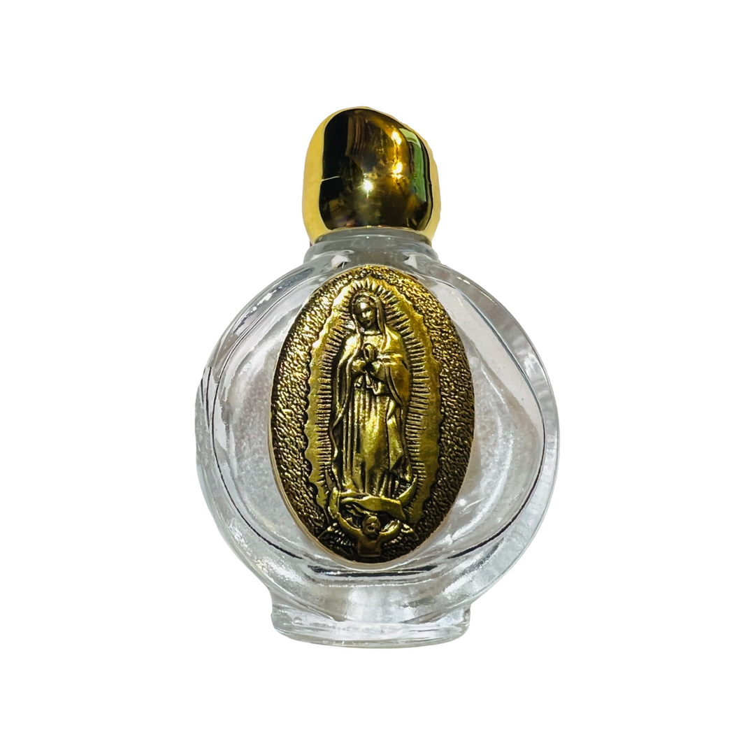 A clear glass bottle with a gold-tone embossed image of Our Lady of Guadalupe on the front. The bottle is topped with a shiny gold cap