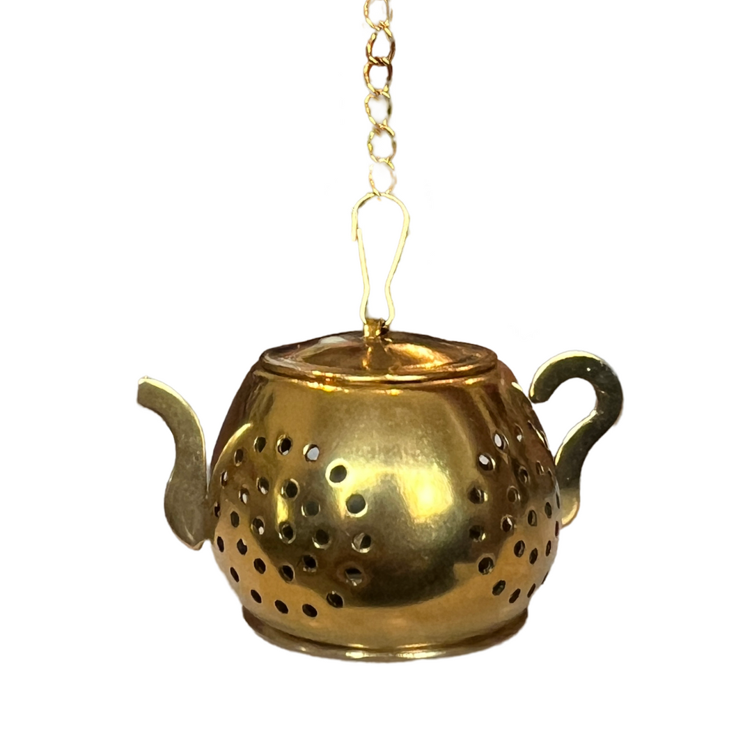  a gold teapot-shaped tea infuser. It features a perforated design and has a small chain 