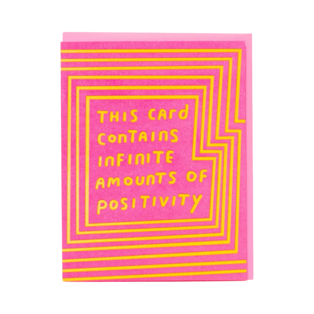 A vibrant pink greeting card with yellow text that reads, "This card contains infinite amounts of positivity," surrounded by geometric yellow lines. Paired with a pink envelope.