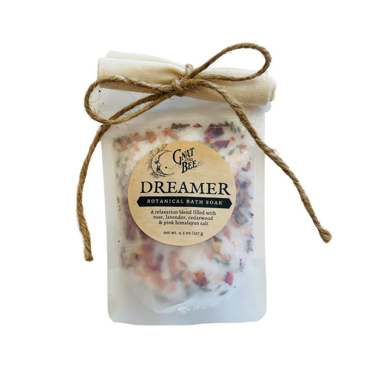 A package of "Dreamer" Botanical Bath Soak by Gnat and Bee, featuring a relaxation blend of rose, lavender, cedarwood, and pink Himalayan salt. The pouch is sealed with a fabric cover and tied with a rustic twine bow.