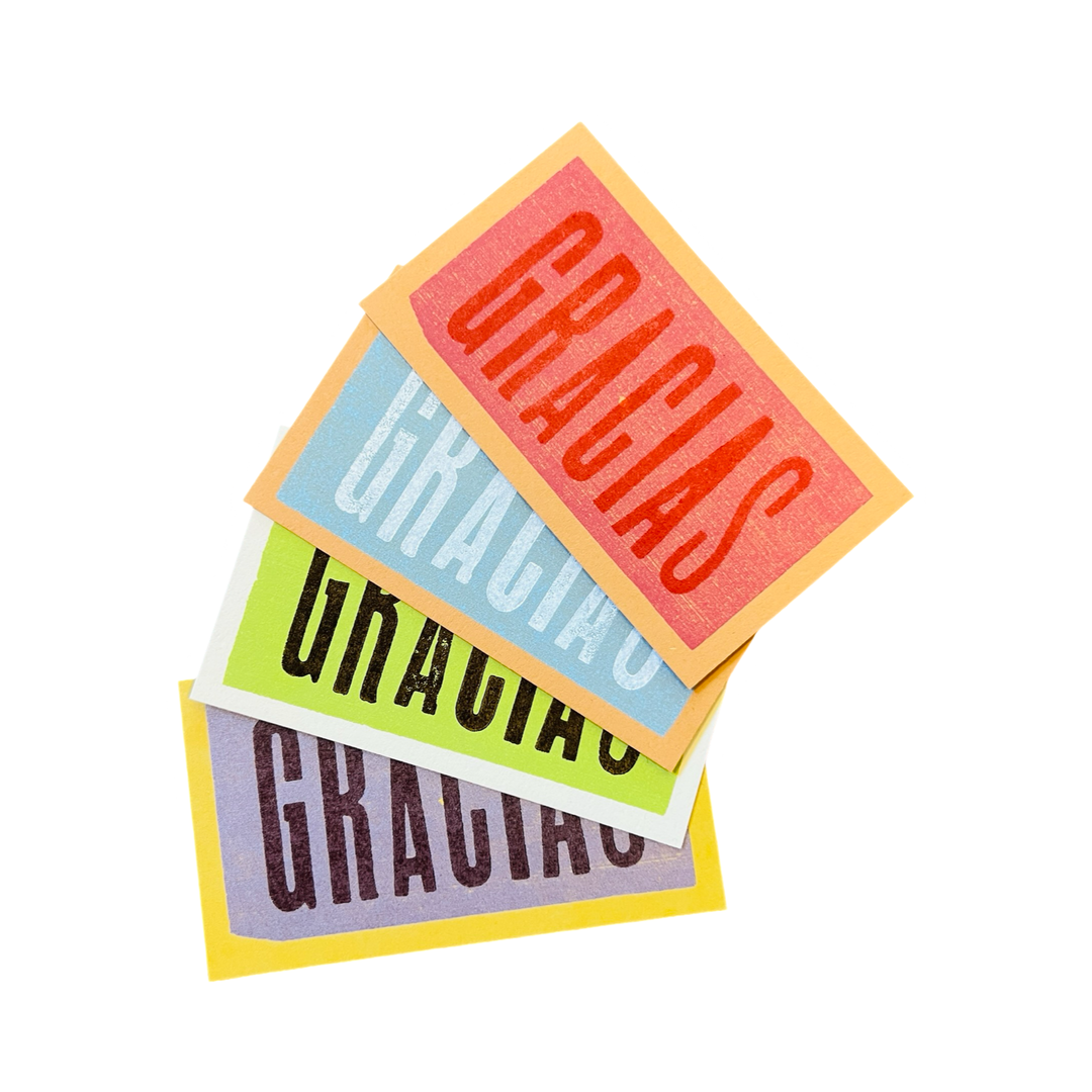 A stack of colorful mini cards with the word "GRACIAS" printed in bold, vintage-style typography. The cards come in a mix of red, blue, green, and yellow hues, creating a vibrant and cheerful expression of gratitude.