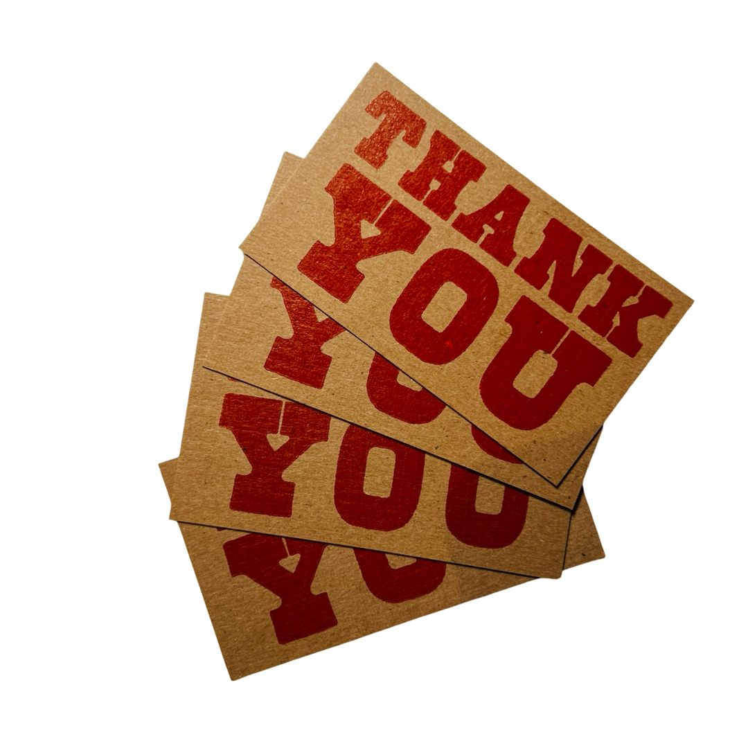 A set of small, flat kraft paper cards with "THANK YOU" printed in bold red ink using a vintage letterpress style. The stacked cards create a layered effect, showcasing the rustic charm of the design.