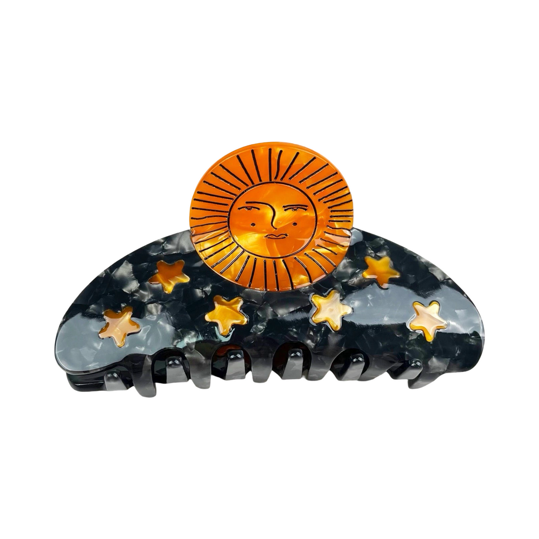 black acrylic hair clip featuring gold stars and a gold sun with a face.