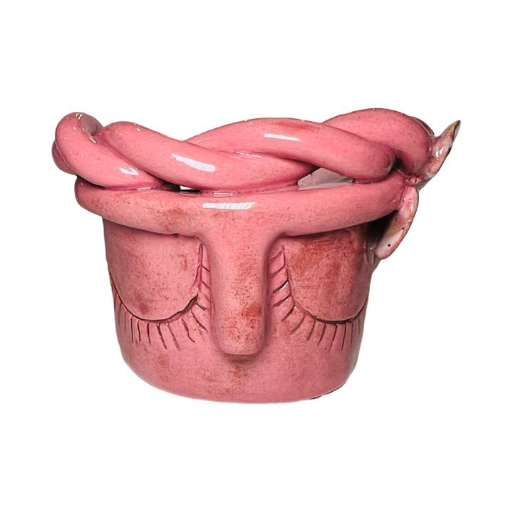 front view of a blush espresso cup made of barro (clay) with a glazed finish, featuring a face design and braided detailing around the rim.