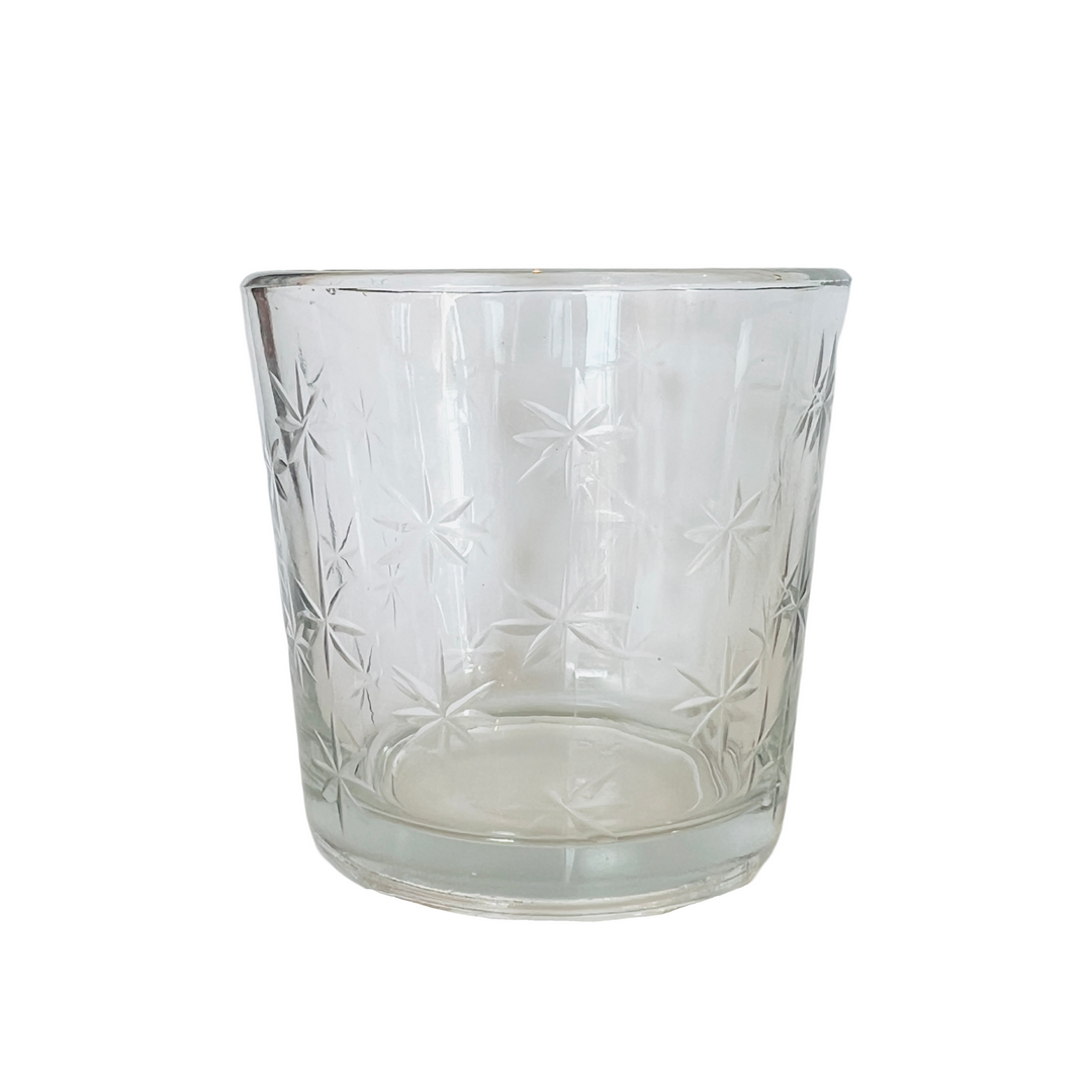 A glass votive cup with delicate star engravings, designed to hold votive candles or tea lights