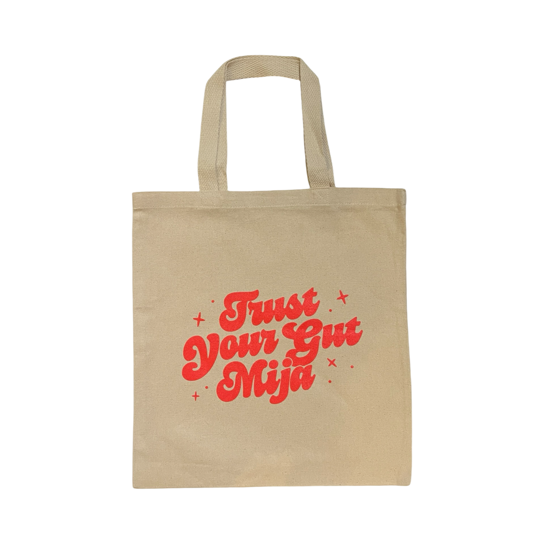 natural canvas tote bag with the phrase Trust your gut mija with neon coral lettering.