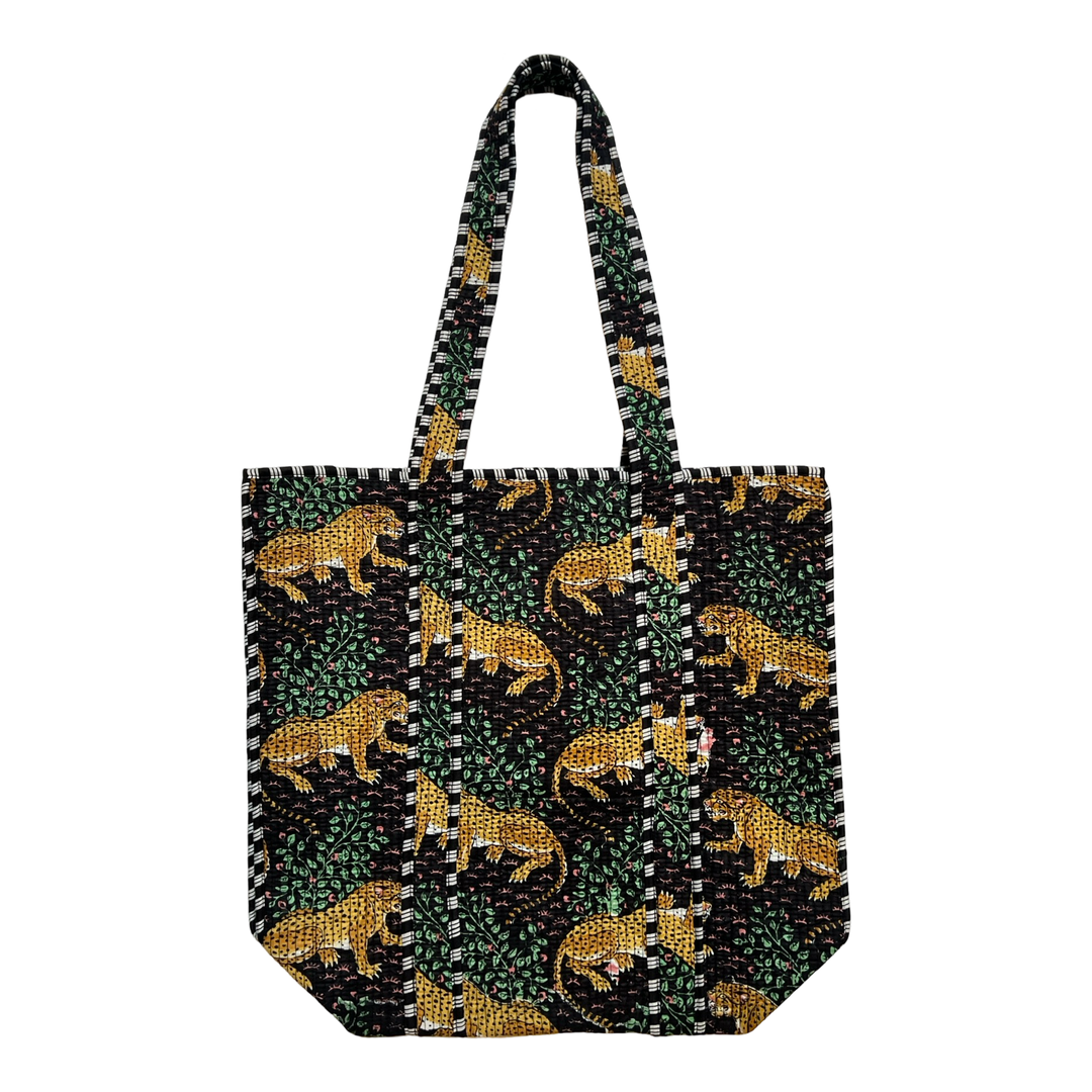 A quilted tote bag featuring a tiger print with greenery on a black background.The bag has two sturdy quilted handles with a matching striped pattern.