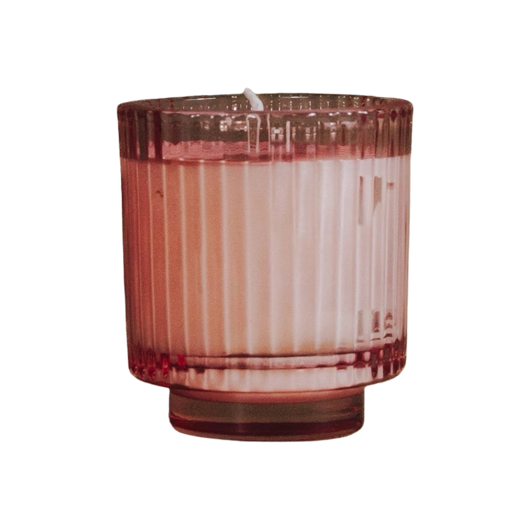 candle in a deep rose pink ribbed glass vessel with a footed base.