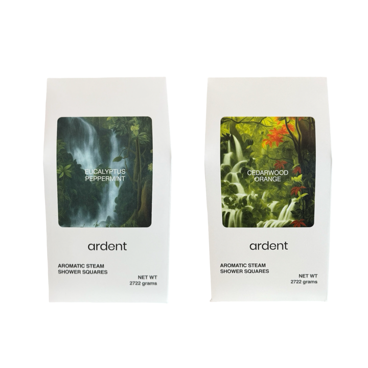 Two white packages of Ardent Aromatic Steam Shower Squares. The left package is labeled “Eucalyptus Peppermint” with a lush waterfall forest image. The right package is labeled “Cedarwood Orange” with a vibrant green forest and orange foliage image. Both packages state a net weight of 272.2 grams.