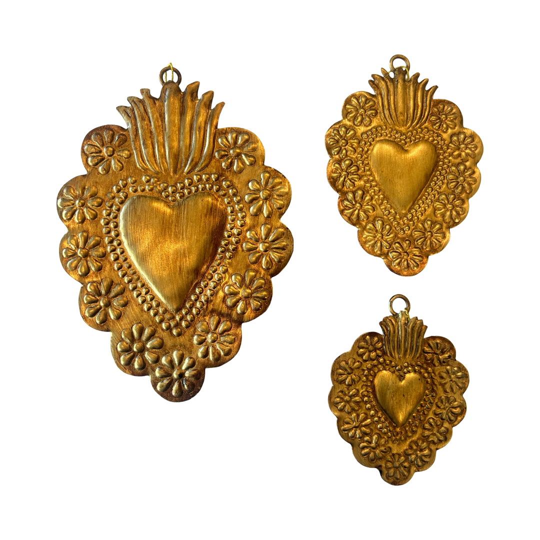 3 brass colored sacred hearts surrounded by a floral design of different sizes.