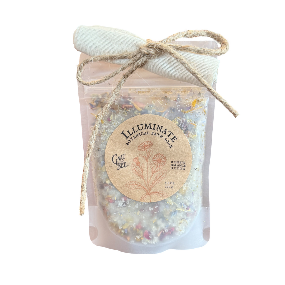4.5 oz frosted pouch with a branded label that features an illustration of flowers along with the product name: Illuminate Botanical Bath Soak. Includes a rolled up fabric on the top, tied with a piece of twine.
