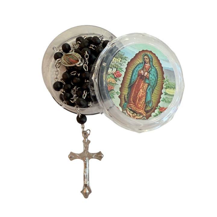 Clear round rosary case with an image of Our Lady of Guadalupe on the lid, shown open with the black bead rosary and silver crucifix partially inside.