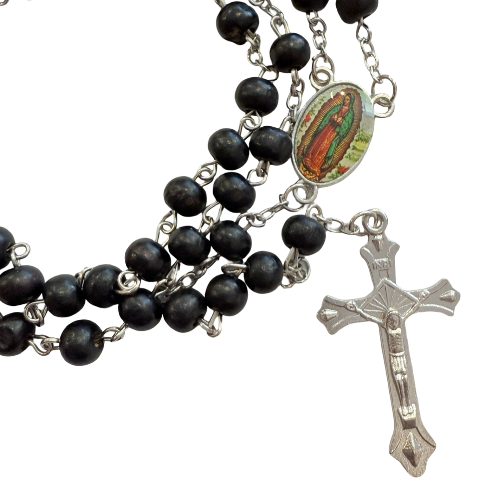 close up view of a Black wooden bead rosary with silver-tone crucifix and an oval Our Lady of Guadalupe centerpiece, coiled on a white background.