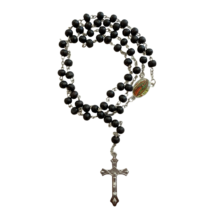 Black wooden bead rosary with silver-tone crucifix and an oval Our Lady of Guadalupe centerpiece, coiled on a white background.