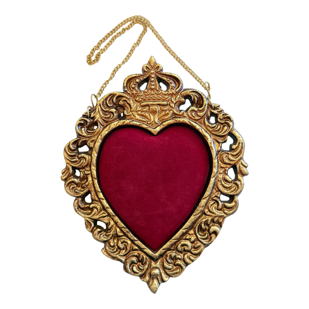An ornate gold-toned hanging frame in the shape of a heart with a rich red velvet center and an intricate crown detail on top.