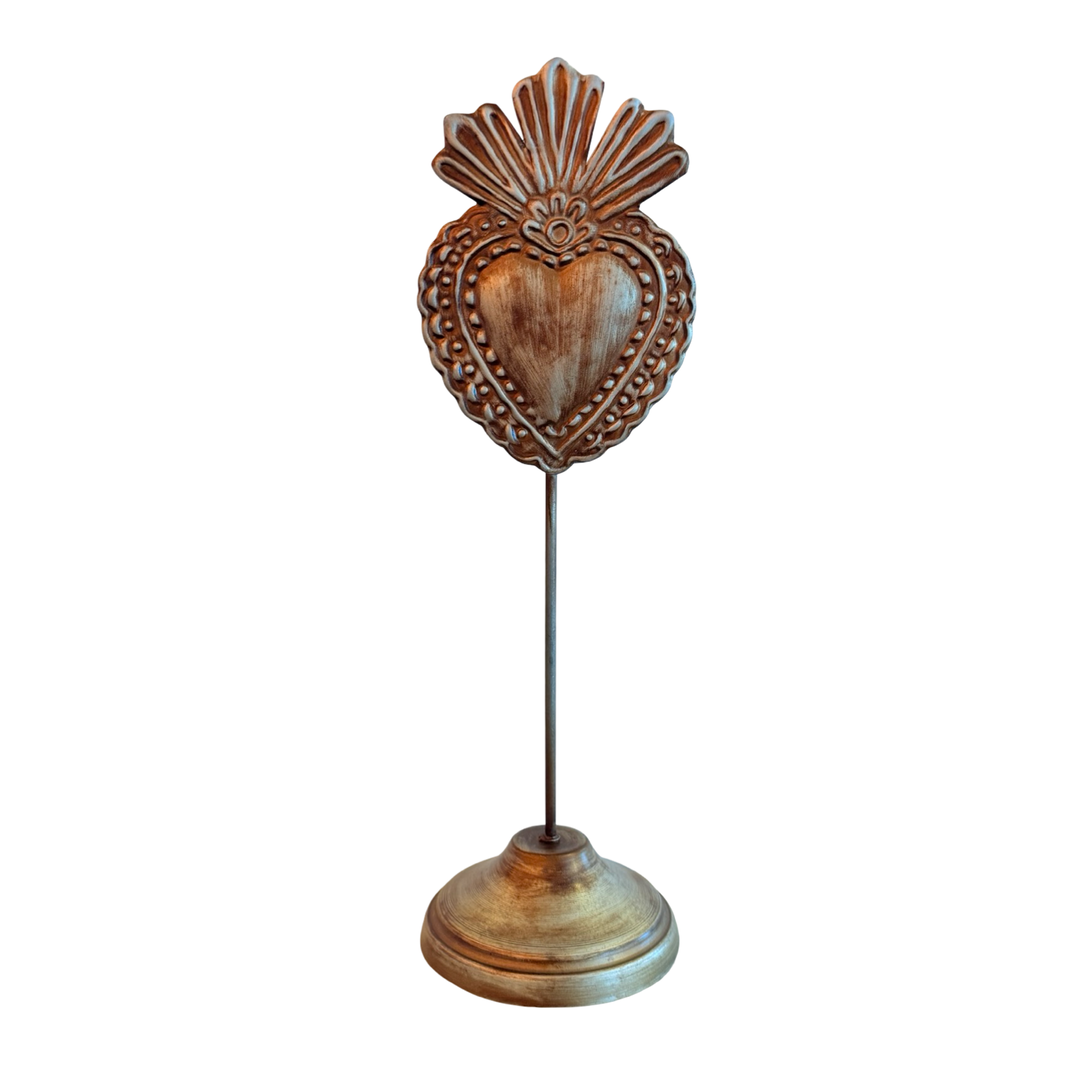A bronze-toned candle holder shaped like a sacred heart with a scalloped design at the top, mounted on a tall stand with a round base.