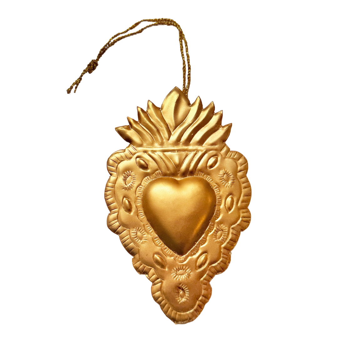 Gold-toned flaming heart milagro ornament with embossed floral details and a gold hanging string.