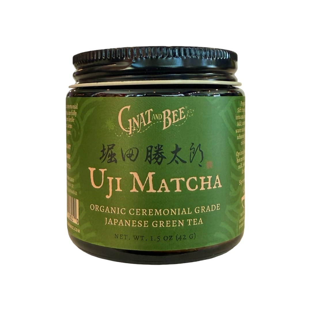 A 1.5 oz  dark glass jar of Gnat and Bee Uji Matcha, organic ceremonial grade Japanese green tea, with a deep green label and gold lettering.