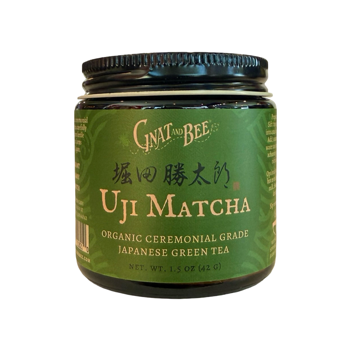 A 1.5 oz  dark glass jar of Gnat and Bee Uji Matcha, organic ceremonial grade Japanese green tea, with a deep green label and gold lettering.