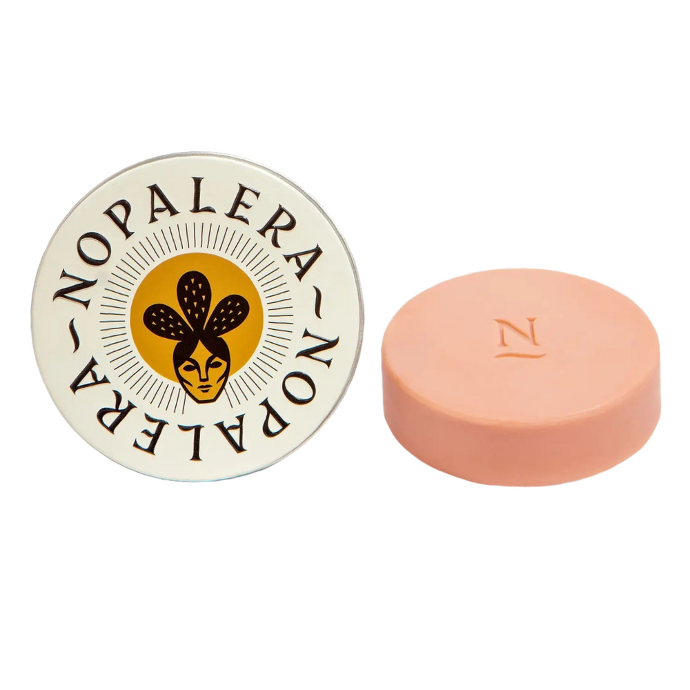 cream round tin with an image of a woman wearing a cactus crown and a blush round lotion bar on the side. Brand: Nopalera