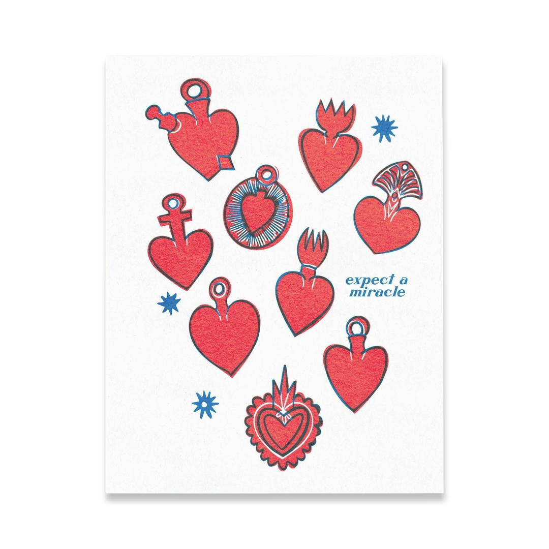 white card with various red milagro hearts and the phrase Expect A Miracle in blue lettering