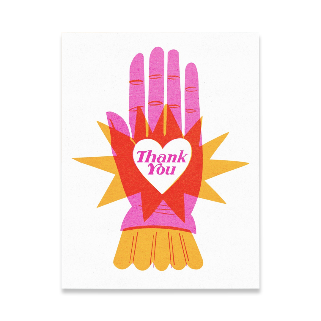 white card with a pink hand, orange star burst and a white heart in the center of the hand featuring the phrase Thank you in pink lettering