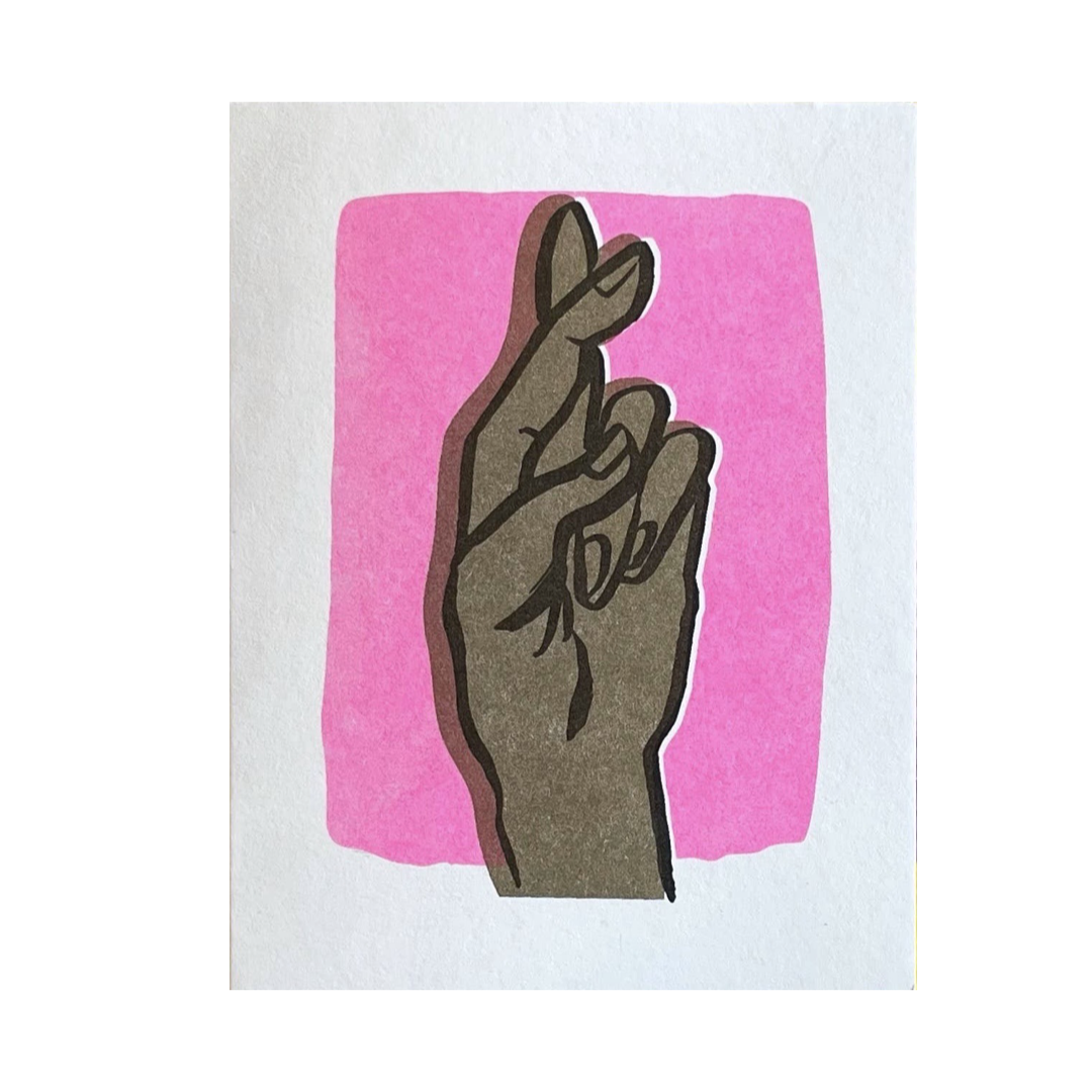 white card with a hand posed in a fingers crossed gesture in front of a pink block