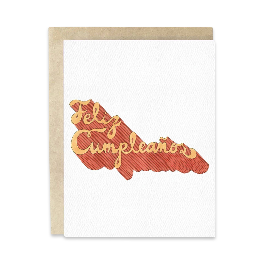 Brown envelope behind a white textured card and the phrase Feliz Cumpleanos in cursive and in two shades of orange lettering