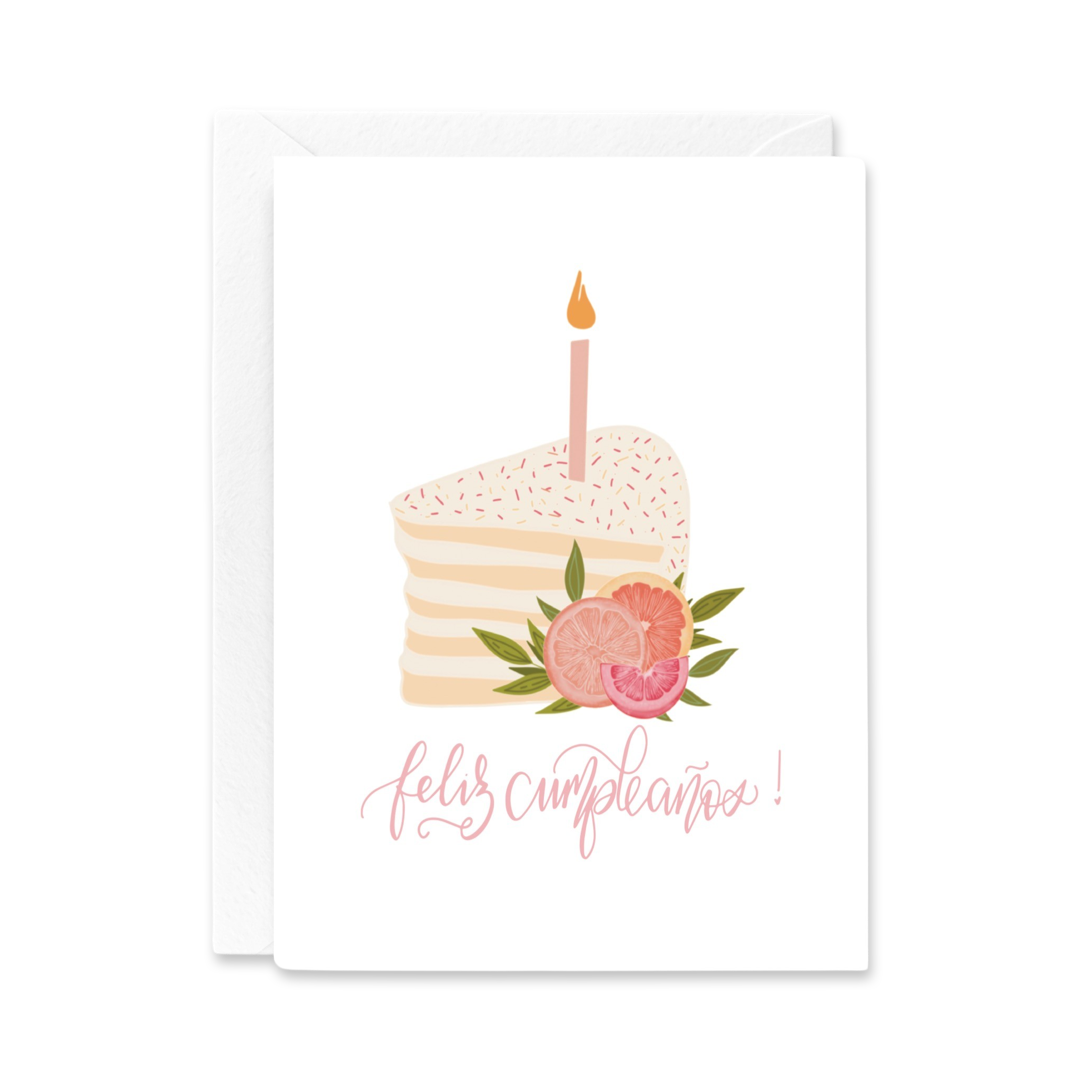 white card with an illustration of a slice of layered cake, a pink candle, slices of pink oranges and the phrase Feliz cumpleanos in pink lettering