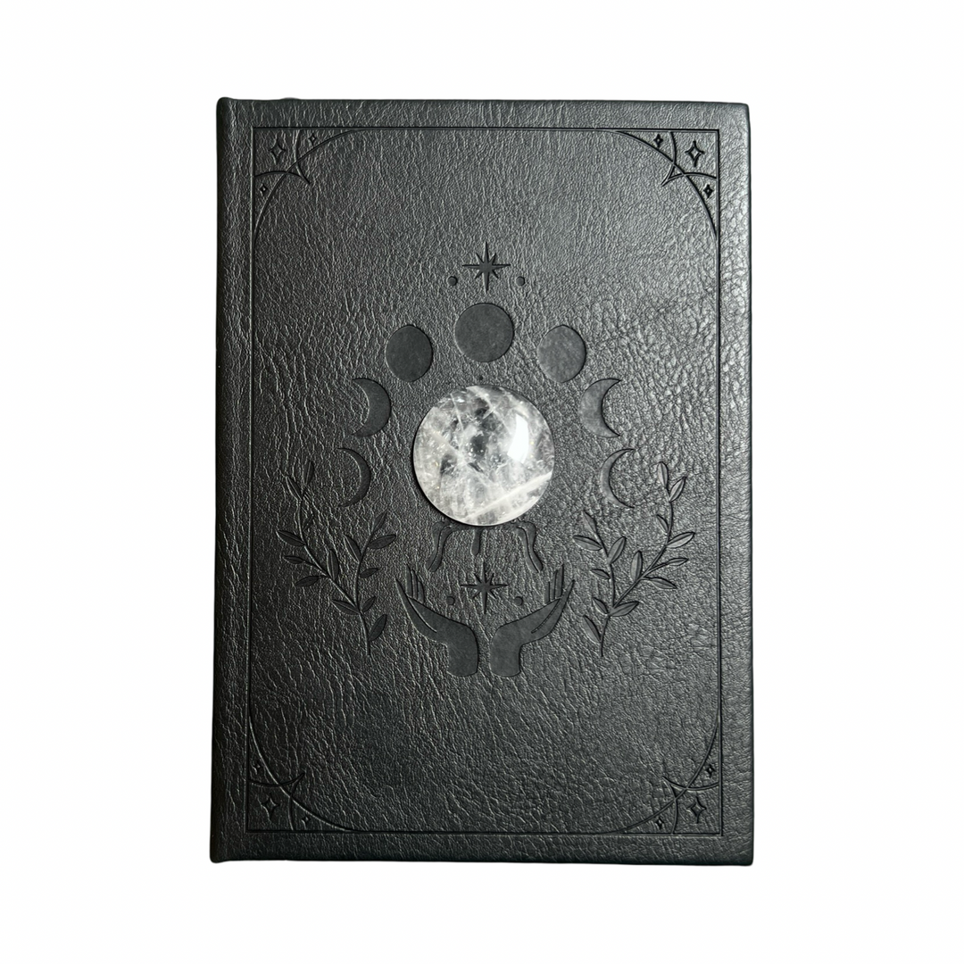 black vegan leather journal with the moon phases embossed on the cover with a round crystal quartz in the center.