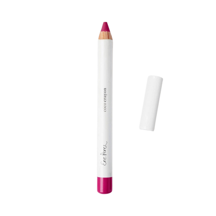 Fuschia lip crayon in white packaging with black lettering and a white lid laying to the right of the crayon.