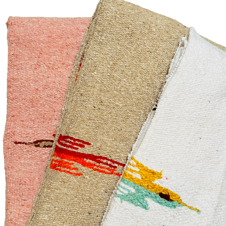 close up of three quarter folded woven blankets in the colors dusty pink, tan and white.