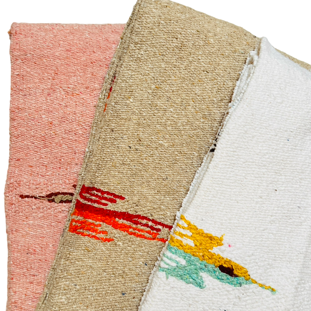 three quarter folded woven blankets with a bird design in the colors dusty pink, tan and white.