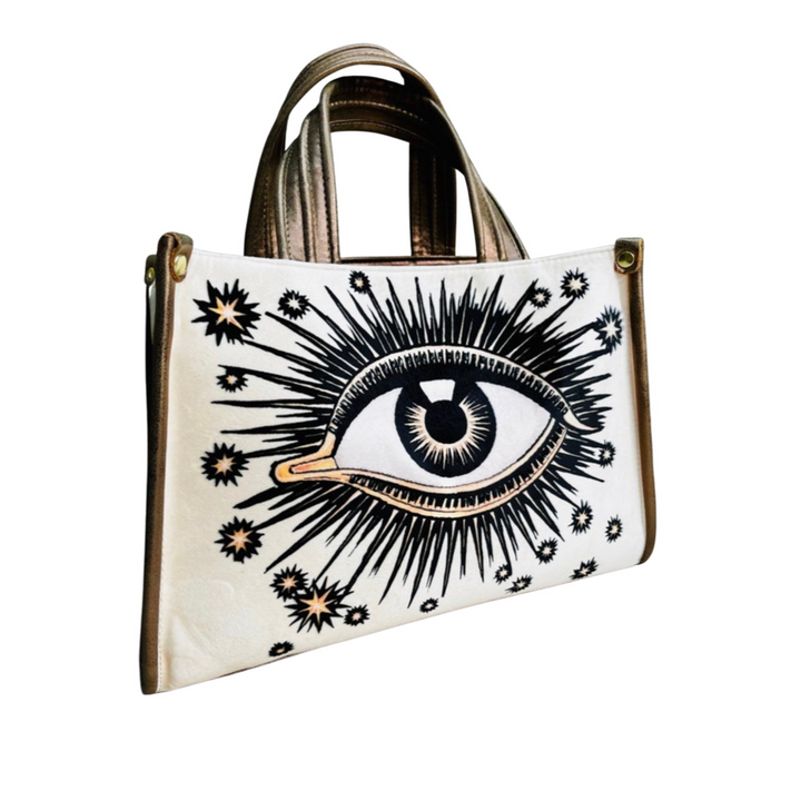 Beige  hand bag with an image of an eye with sunbursts and sun rays. Brand: La Funky Mexicana